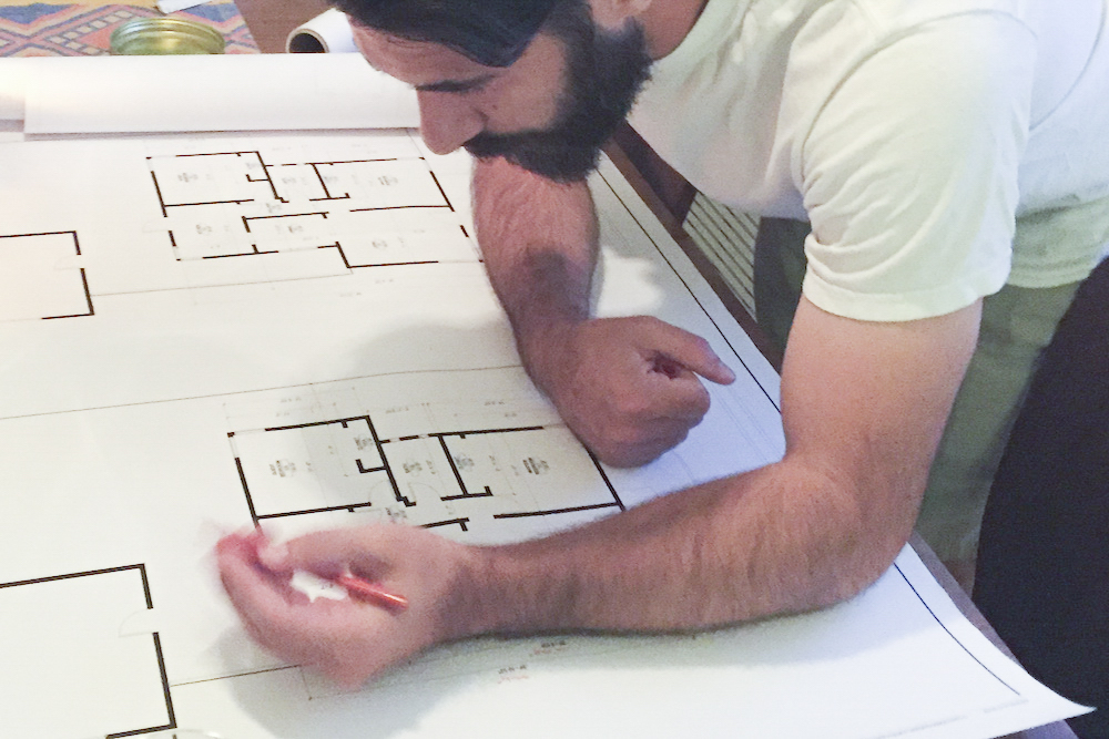 young man leaning over a set of printed plans with pencil